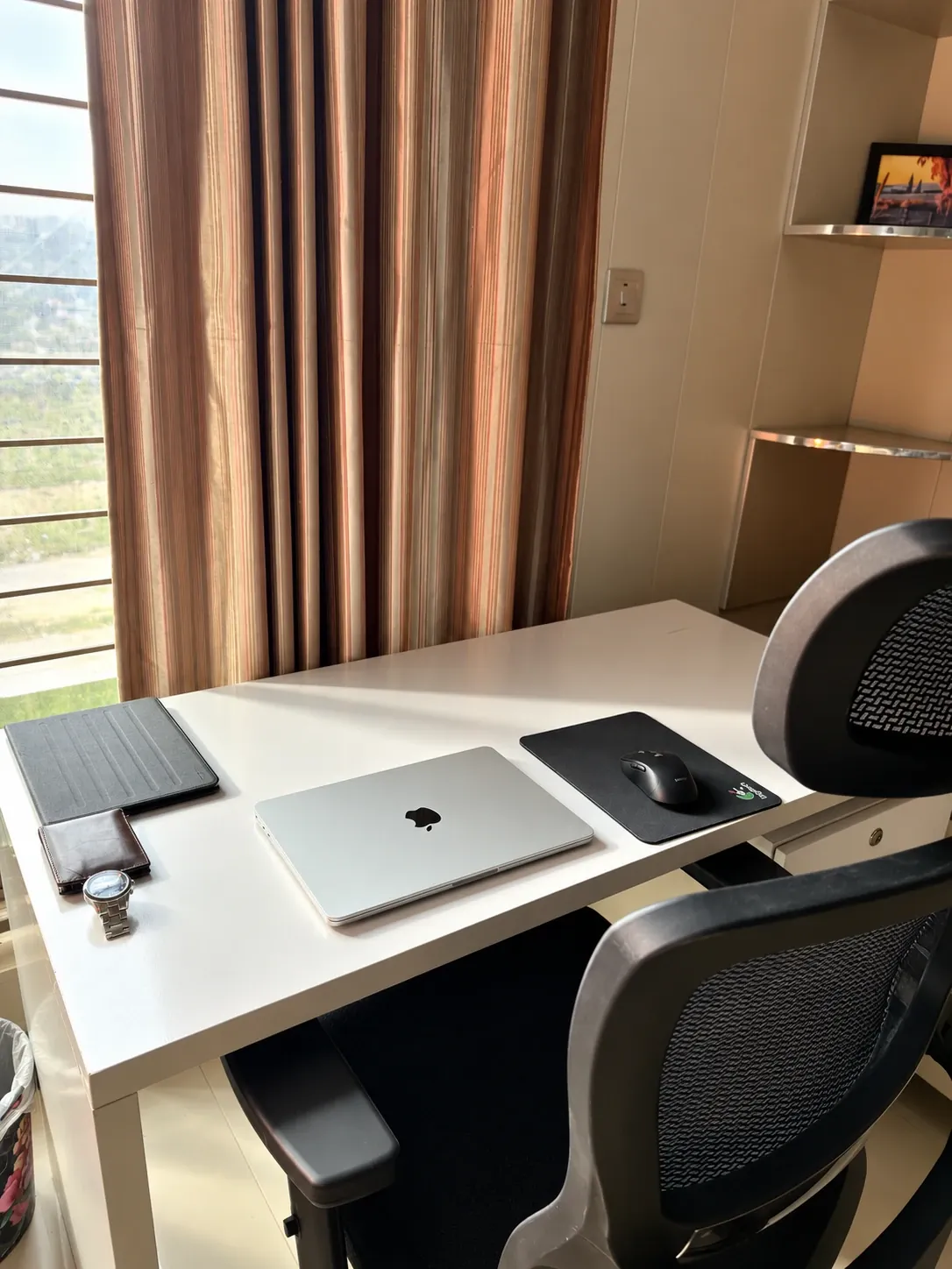 Desk by a window with a laptop, mouse and office chair